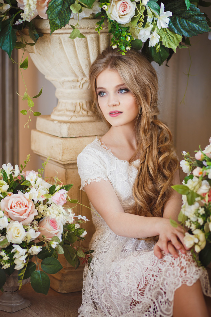 Portrait of pretty young girl in a white dress and long blonde hair surrounded by flowers - Φωτογραφία, εικόνα