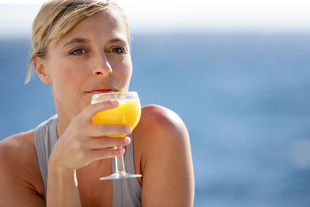 γυναίκα απολαμβάνοντας ποτήρι χυμό πορτοκαλιού, δίπλα στη θάλασσα - Φωτογραφία, εικόνα