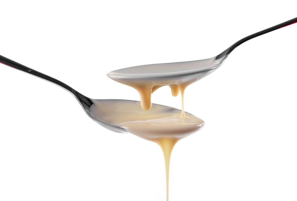 Condensed milk pouring from spoons, isolated on white - Photo, Image