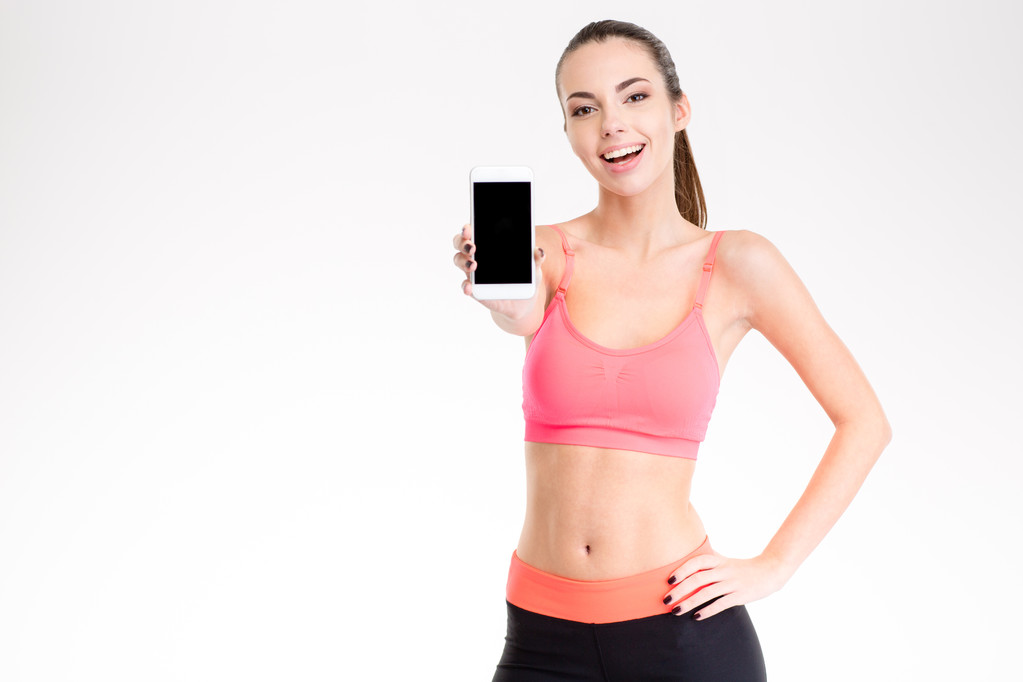Atractiva mujer joven y alegre fitness mostrando la pantalla del teléfono inteligente en blanco
 - Foto, Imagen