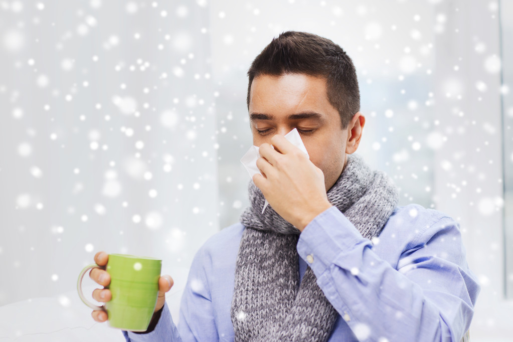 zieke man met griep drinken thee en blazen neus - Foto, afbeelding