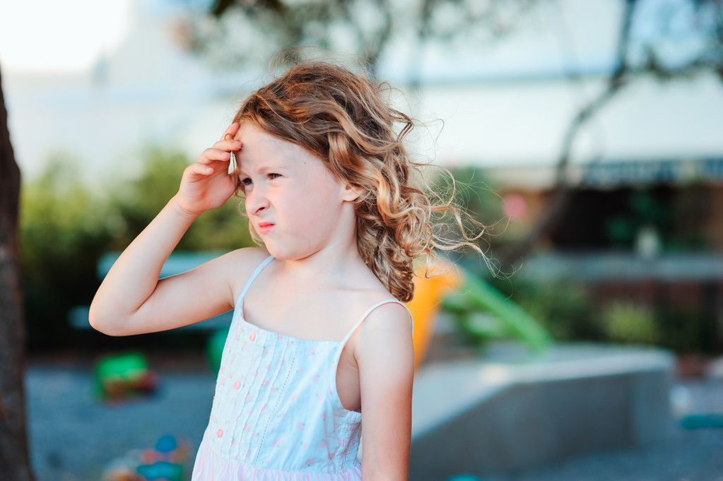 sad child girl with headache on summer playground, touching head - Photo, Image
