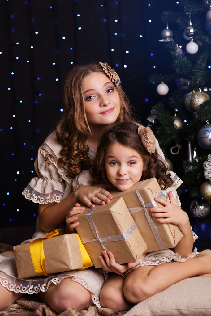 Duas meninas amigas com presentes perto da árvore de Natal
 - Foto, Imagem