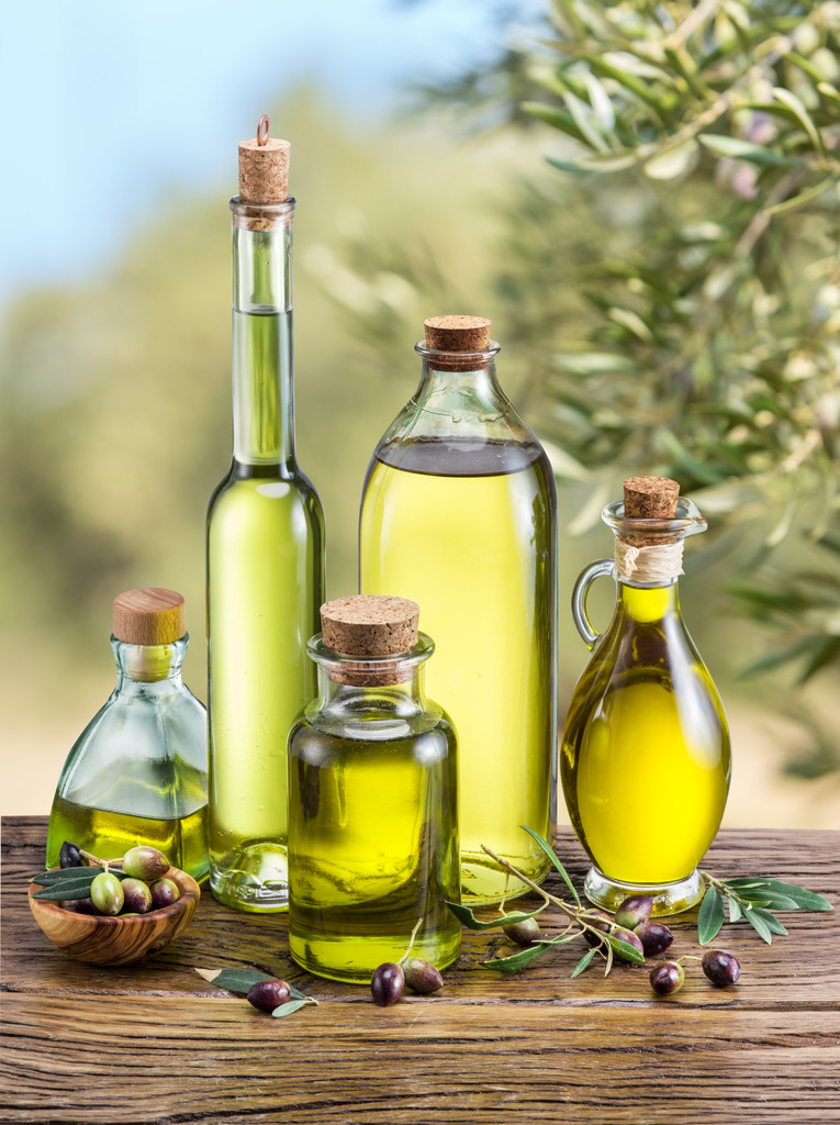 Olivenöl und Beeren liegen auf dem Holztisch unter dem Olivenbaum. - Foto, Bild