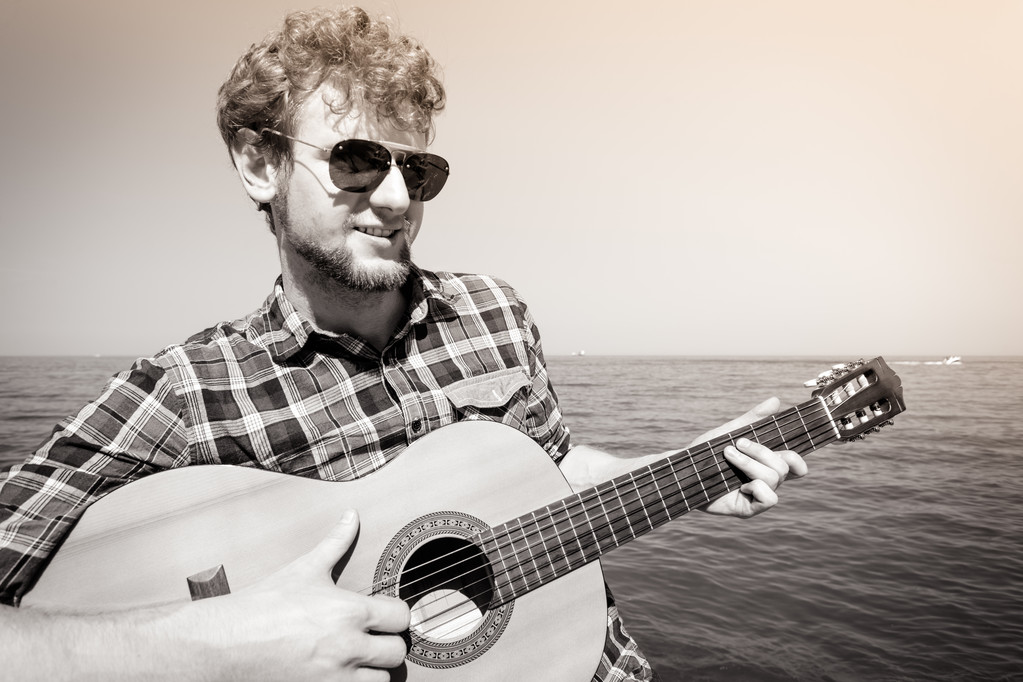 Nuori mies hipster soittaa kitaraa meren rannalla
. - Valokuva, kuva