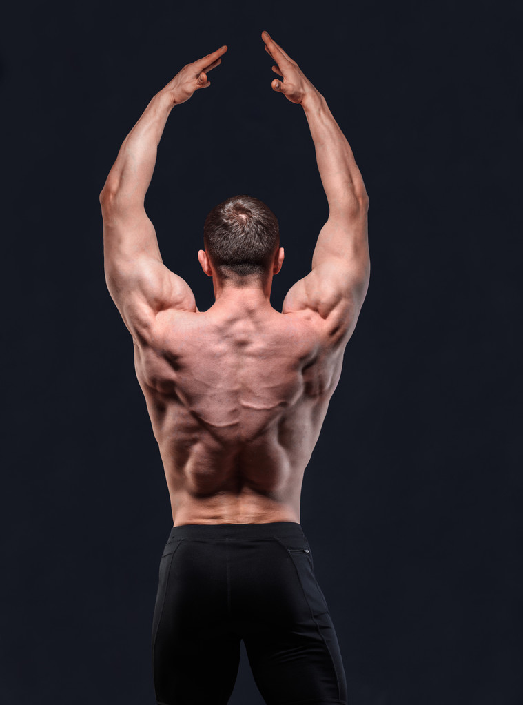 Мускулистый мужчина в студии показывает спину с высоко поднятыми руками
 - Фото, изображение