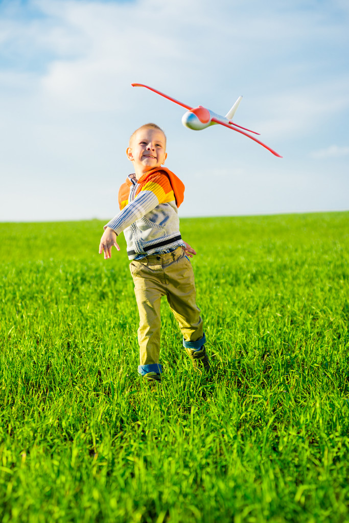 Ευτυχισμένο παιδί παίζει με αεροπλάνο παιχνίδι φόντο μπλε καλοκαιρινό ουρανό και πράσινη πεδίο. - Φωτογραφία, εικόνα