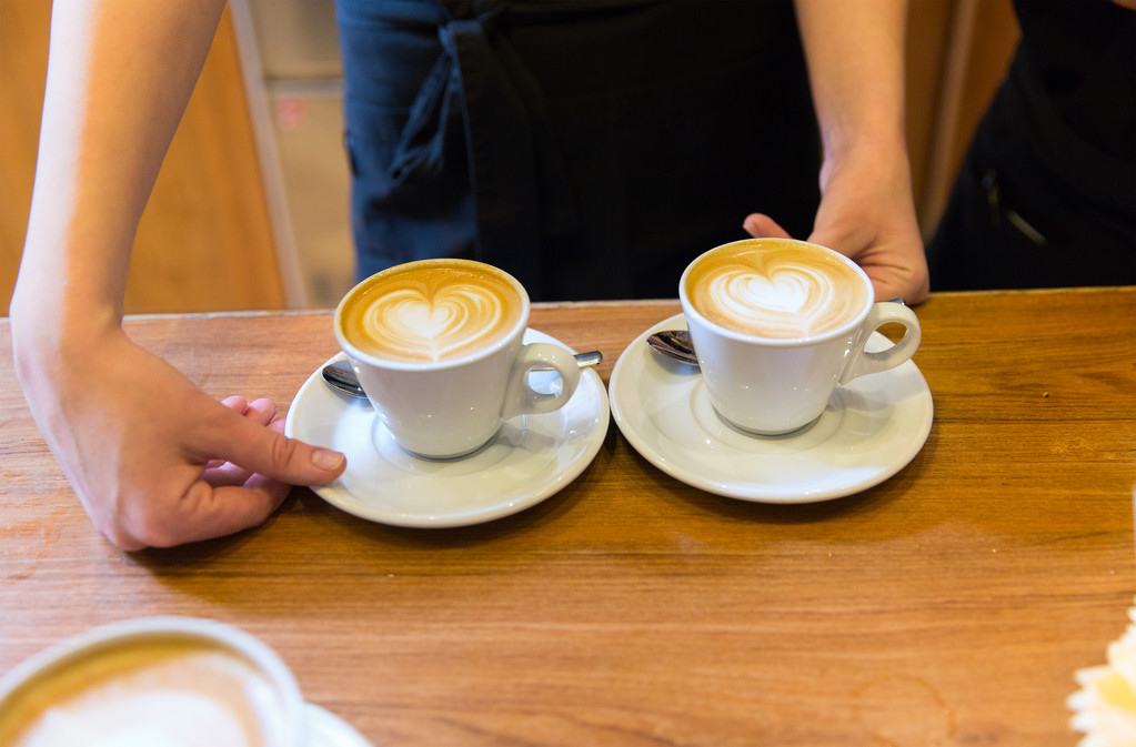 τα χέρια με την τέχνη latte στο φλιτζάνι καφέ σε κοντινό πλάνο - Φωτογραφία, εικόνα