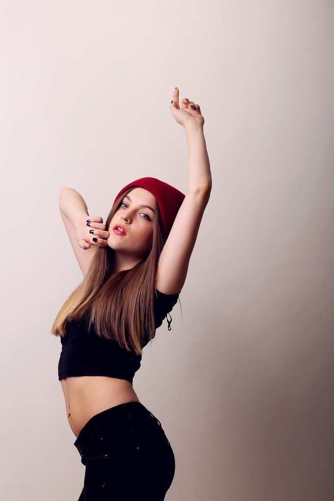 ευτυχισμένος κορίτσι στέκεται σε ένα στούντιο σε μπεζ φόντο, καπάκι στο κεφάλι, μοντέλο Ποζάροντας, κόκκινα χείλη - Φωτογραφία, εικόνα