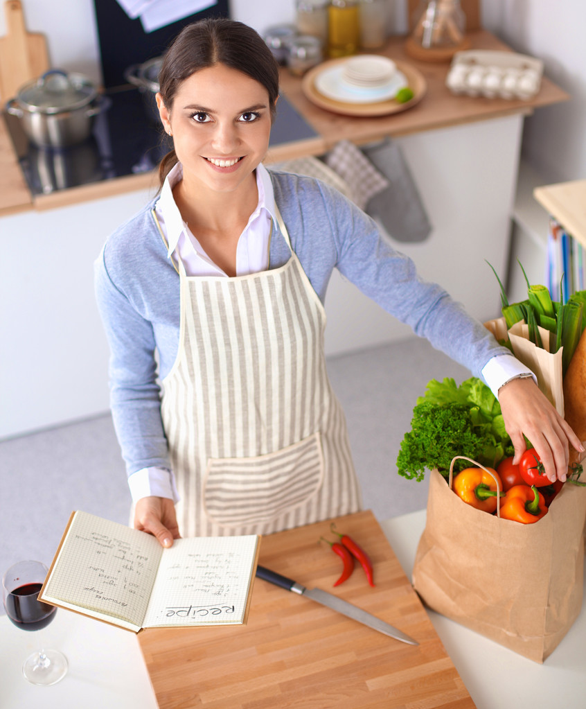 Mulher fazendo comida saudável em pé sorrindo na cozinha
 - Foto, Imagem