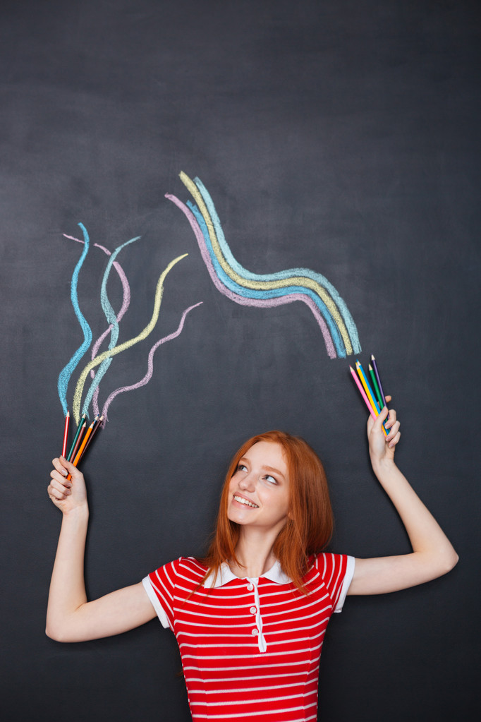 Happy woman holding colorful pencils and drawing on chalkboard background - Fotografie, Obrázek
