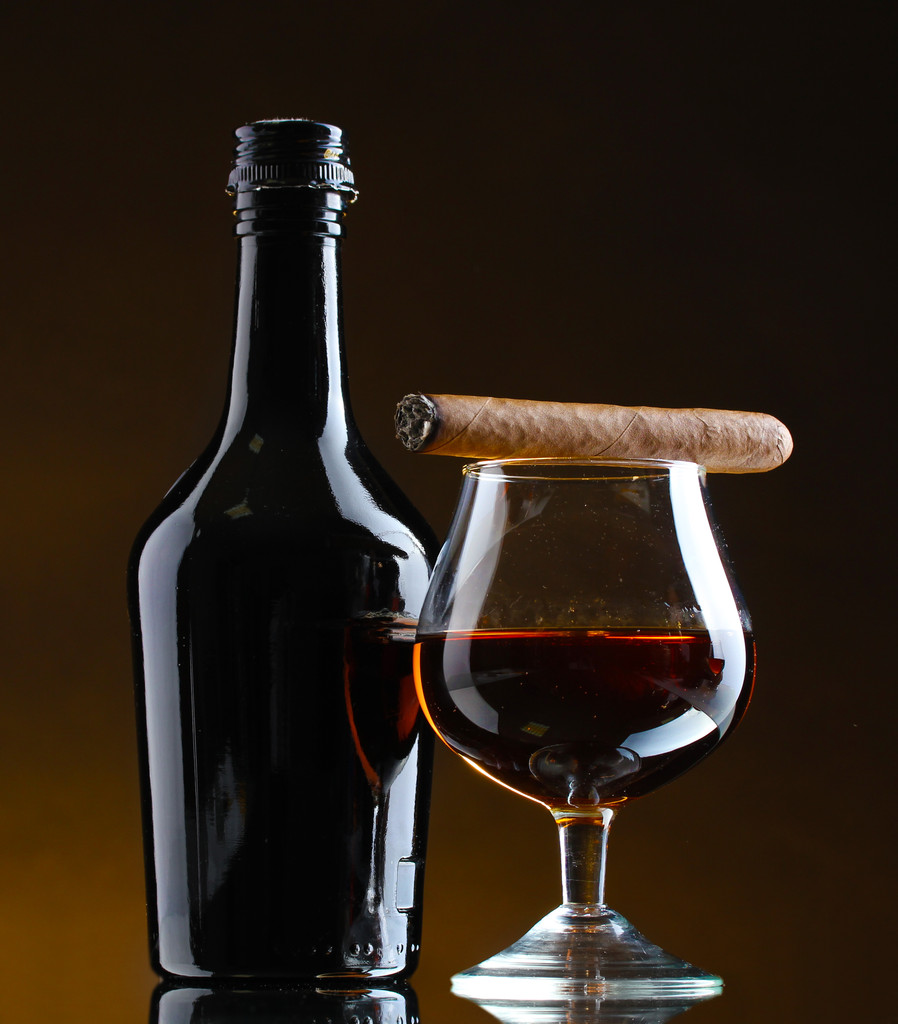 şişe ve bardak brendi ve puro kahverengi zemin üzerinde - Fotoğraf, Görsel