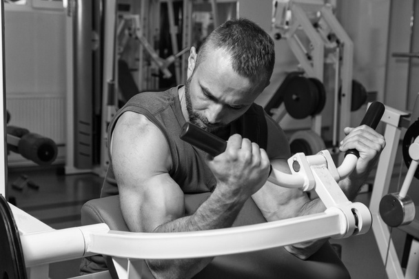 The athlete does bench biceps on the simulator in the gym. Hand muscle training on the simulator. Tense muscles of hands under load. Photos for sporting magazines, posters and websites. - Photo, Image