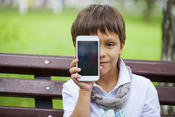 A little boy sits on a bench and calling by mobile phone  - Foto, Imagem