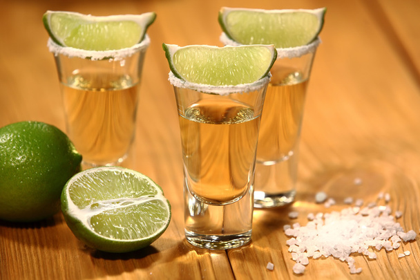 Three short glasses with alcohol next to a slice of lime and salt are on an old rustic table with vintage texture - Photo, Image