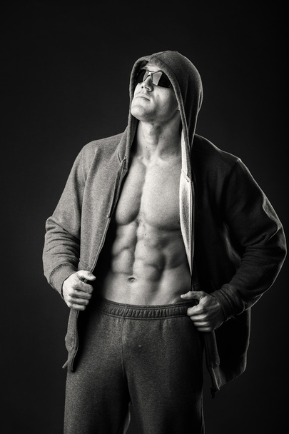 Muscled man in a sports jacket and dark glasses on a black background. Demonstration body muscles during sports jacket. Sportswear and accessories. Photos for sporting magazines and websites. - Fotoğraf, Görsel