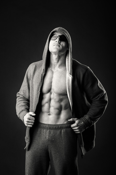 М'язистий чоловік у спортивній куртці та темних окулярах на чорному тлі. Демонстрація м'язів тіла під час спортивного піджака. Спортивний одяг та аксесуари. Фотографії для спортивних журналів і веб-сайтів
. - Фото, зображення