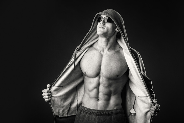 muskulöser Mann in Sportjacke und dunkler Brille auf schwarzem Hintergrund. - Foto, Bild
