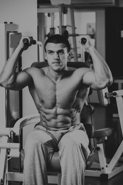Сильний м'язистий чоловік робить вправи в тренажерному залі. Красиве тіло на чорно-білому фото. Здоровий спосіб життя
. - Фото, зображення