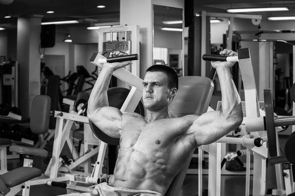Hombre musculoso fuerte haciendo ejercicios en el gimnasio. Hermoso cuerpo en una foto en blanco y negro. Estilo de vida saludable
. - Foto, imagen