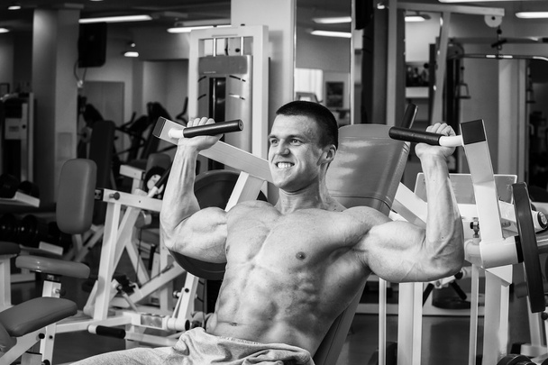 Hombre musculoso fuerte haciendo ejercicios en el gimnasio. Hermoso cuerpo en una foto en blanco y negro. Estilo de vida saludable
. - Foto, Imagen