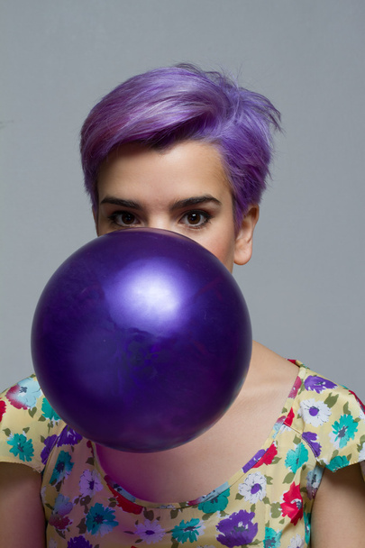 Violeta mujer de pelo corto sosteniendo un globo con la boca, mira
 - Foto, imagen