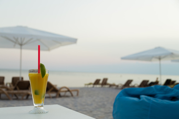 A glass of juice on white table. Relax on the beach. A delicious refreshing drink. Beautiful views of the sea. Photo for travel and social magazines, posters, backgrounds and websites. - Fotografie, Obrázek