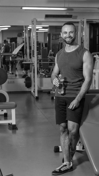 Un homme fort dans la salle de gym. Repos entre les exercices. Un bel homme boit de l'eau
. - Photo, image
