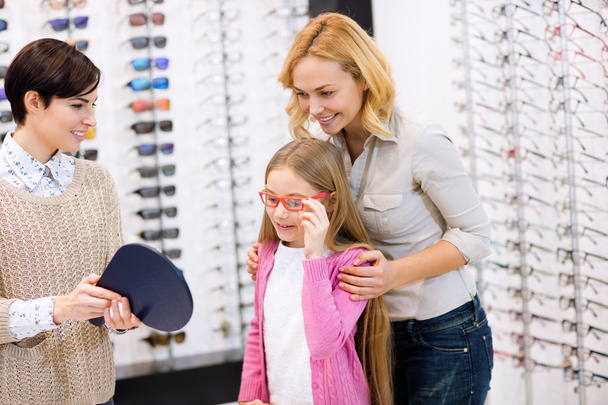 Saleswoman hold mirror while child try frames for eyeglasses - Fotoğraf, Görsel