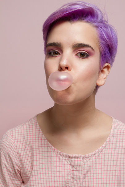 Violet short-haired woman in pink pastel, blowing a bubble with  - Foto, Imagen
