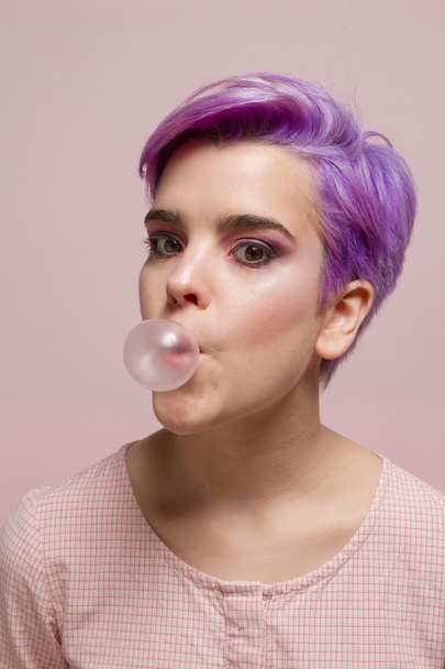 Violet short-haired girl in pink pastel, blowing a bubble gum ba - Photo, Image
