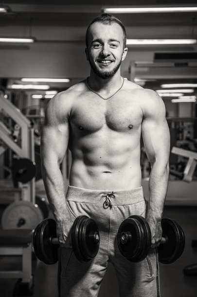 Man at the gym. Man makes exercises dumbbells. Sport, power, dumbbells, tension, exercise - the concept of a healthy lifestyle. Article about fitness and sports. - Fotó, kép