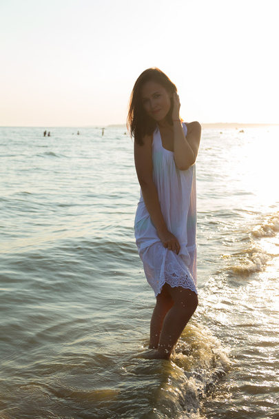 The young beautiful girl in a white dress on the beach. Photo beautiful girl on the beach. Girl posing in seductive manner. Photo for travel and social magazines, posters and websites. - Фото, изображение