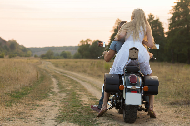 Jeunes mariés au milieu du terrain sur une route de moto. Heureux couple voyageant sur une moto
. - Photo, image