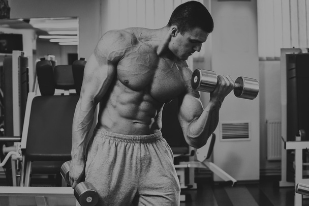 Bodybuilder makes exercise with dumbbells at the gym. - Photo, Image