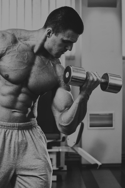Bodybuilder makes exercise with dumbbells at the gym. - Foto, imagen