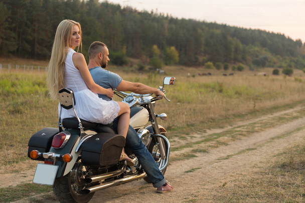 Fiatal szerelmespár egy mezőben egy motorkerékpár - Fotó, kép