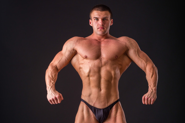 Professional bodybuilder shows his body on a dark background. Muscular body athlete. The result achieved by training and hard work on themselves. Photos for sporting magazines, posters and websites. - Photo, Image