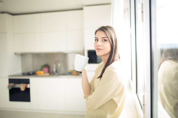 Woman enjoying,holding cup of hot beverage,coffee or tea.Enjoying her morning coffee in the kitchen.Savoring a cup of coffee in bliss and appreciation - Foto, imagen