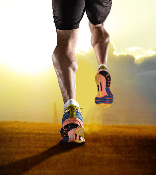 Füße aus nächster Nähe mit Laufschuhen und kräftigen athletischen Beinen des Sportlers beim Joggen im Fitness-Training Sonnenuntergangstraining - Foto, Bild