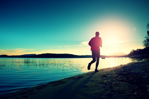Силуэт спортивного активного мужчины бегущего и упражняющегося на пляже на закате
. - Фото, изображение