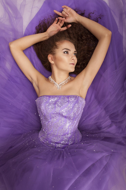 Portrait of a beautiful girl in a purple dress lying on the floor - 写真・画像