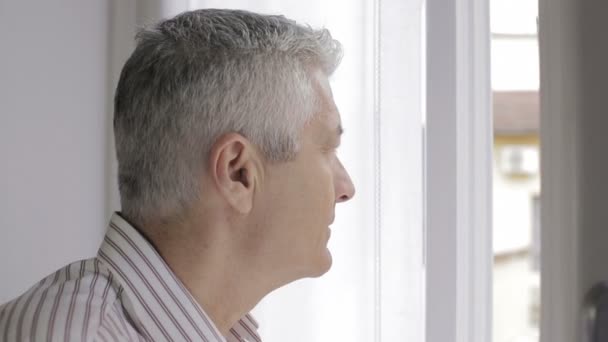 thoughtful man open the window and looks outside: pensive, sunlight, sad, lonely - Video