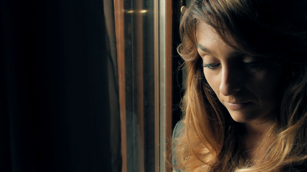 Piękna, smutna dziewczyna tęskni okna - Materiał filmowy, wideo