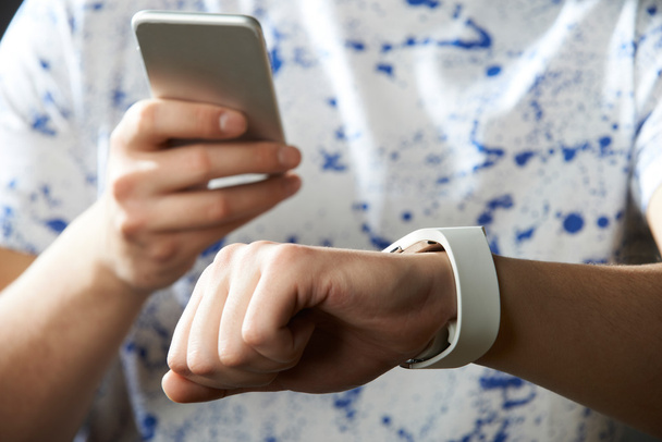 Молодой человек синхронизирует умные часы с мобильным телефоном
 - Фото, изображение