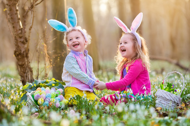 Crianças na caça ao ovo de Páscoa no jardim de primavera florescendo
 - Foto, Imagem