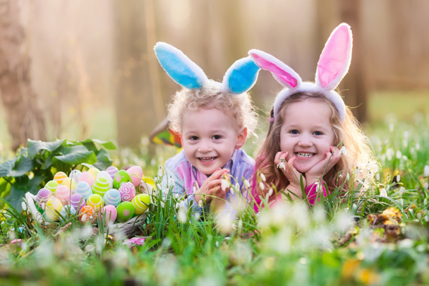 Kinderen op eieren zoeken met Pasen in de bloeiende lente tuin - Foto, afbeelding