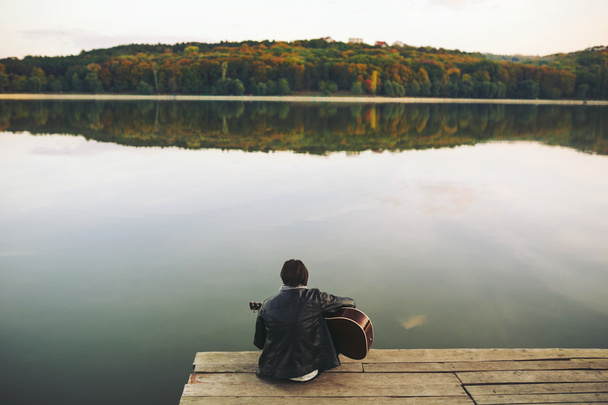 Młody mężczyzna grający na gitarze nad jeziorem - Zdjęcie, obraz