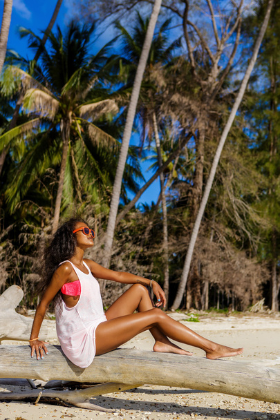 Beautiful teenage black girl sit on palm tree at the beach. - Valokuva, kuva