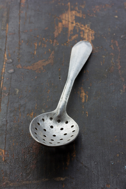 vintage aluminum spoon with holes on an old battered black table closeup. selective focus - Foto, Imagem